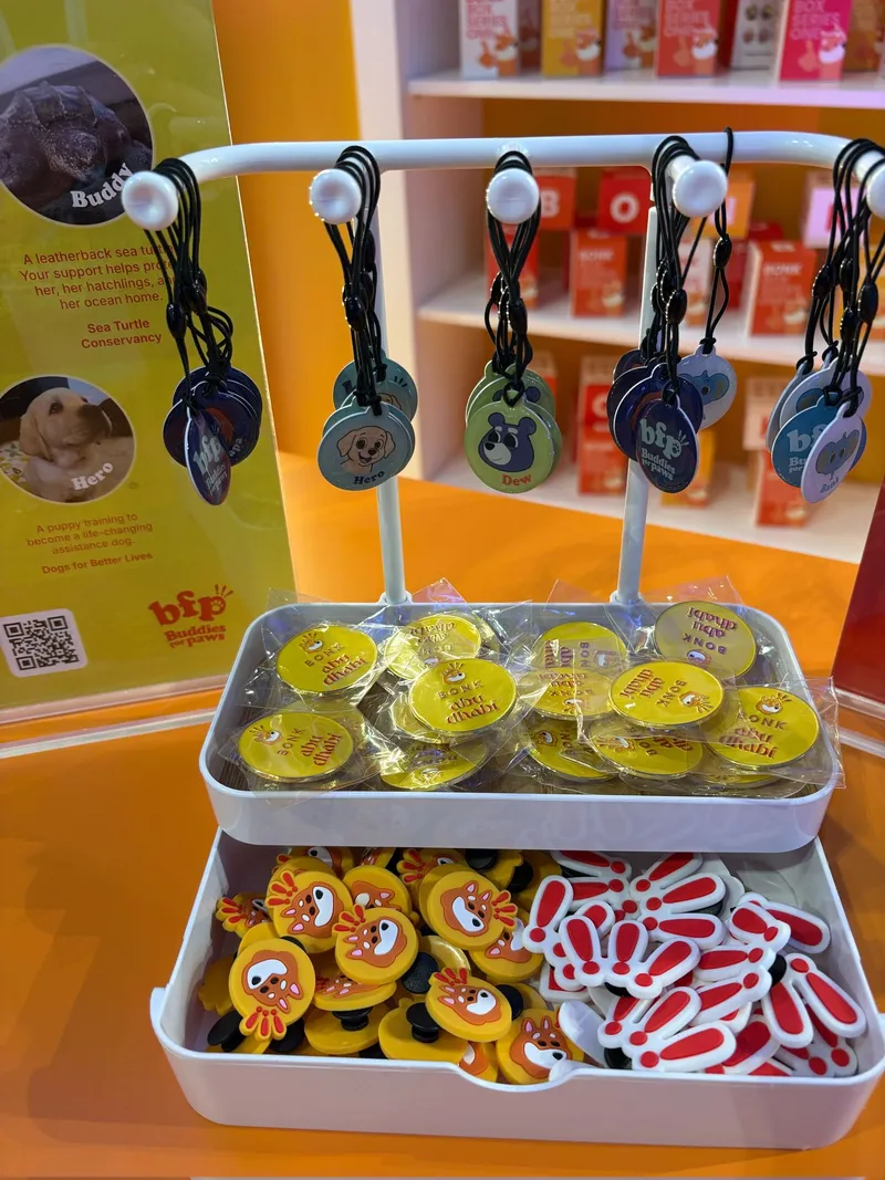 Buddies for Paws NFC keychains hanging from a white stand above trays of keychains